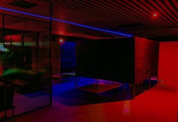 Interior of Kuma Club, a gay bathhouse in Las Vegas. Features include private rooms, a lounge area, and colorful red and blue lighting.
