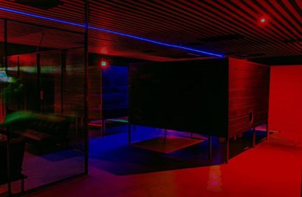 Interior of Kuma Club, a gay bathhouse in Las Vegas. Features include private rooms, a lounge area, and colorful red and blue lighting.