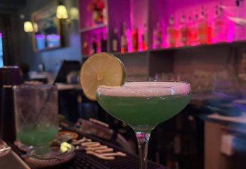 Kween Bar cocktails in Montreal. A green cocktail with a lime garnish on the bar. Gay bar nightlife in Montreal's gay village.