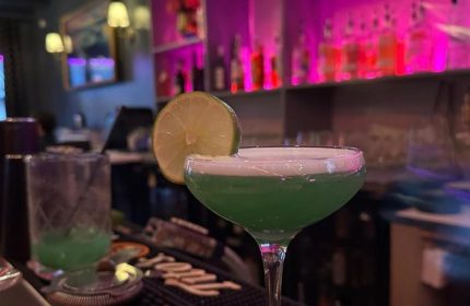 Kween Bar cocktails in Montreal. A green cocktail with a lime garnish on the bar. Gay bar nightlife in Montreal's gay village.