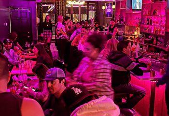 Inside Kween Montreal's kitchen & cocktail bar, patrons enjoy drinks under pink lighting. Popular gay bar for Montreal nightlife.