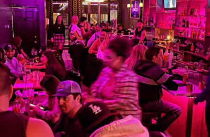 Inside Kween Montreal's kitchen & cocktail bar, patrons enjoy drinks under pink lighting. Popular gay bar for Montreal nightlife.