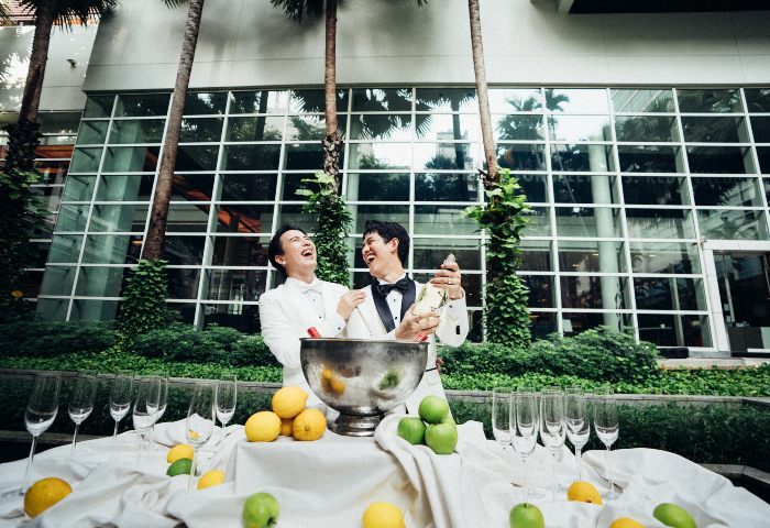 Bangkok King Power Pullman LGBTQ wedding. Two grooms open champagne, celebrating their gay wedding in Bangkok, Thailand.