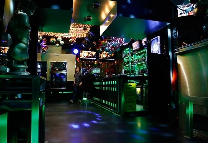 Inside LL Bar, a gay bar in Madrid. Green lighting, disco balls, and a statue create a vibrant atmosphere for gay men travelers.