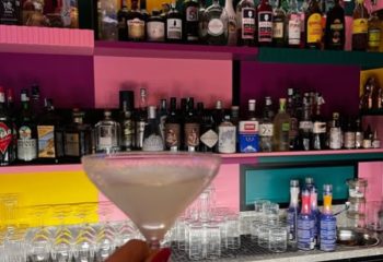 LOLA Milan bar: cocktail in a martini glass, colorful shelves with liquor bottles. Gay travel advice, nightlife in Milan, Italy.
