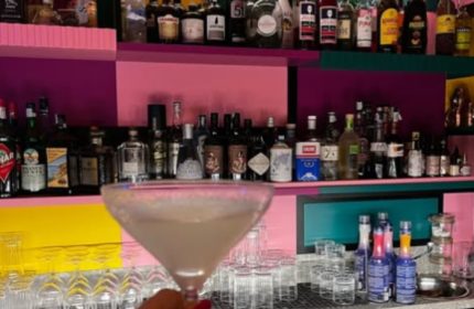LOLA Milan bar: cocktail in a martini glass, colorful shelves with liquor bottles. Gay travel advice, nightlife in Milan, Italy.