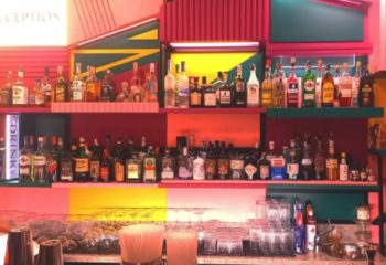 LOLA Milan bar interior. Shelves of liquor bottles behind a bar with glasses. Gay travel advice, Milan nightlife.