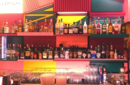 LOLA Milan bar interior. Shelves of liquor bottles behind a bar with glasses. Gay travel advice, Milan nightlife.