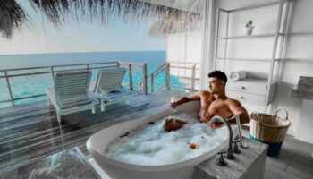 Gay honeymoon at LUX* South Ari Atoll, Maldives. Two men in a bubble bath with ocean view from water villa. Luxury travel destination.