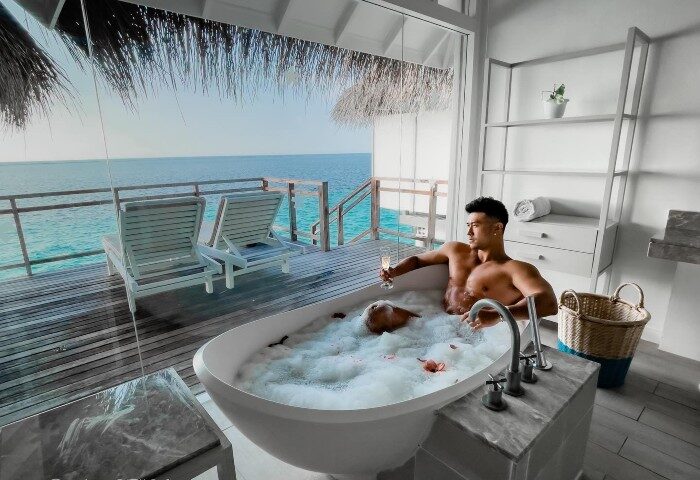 Gay honeymoon at LUX* South Ari Atoll, Maldives. Two men in a bubble bath with ocean view from water villa. Luxury travel destination.