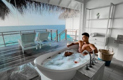 Gay honeymoon at LUX* South Ari Atoll, Maldives. Two men in a bubble bath with ocean view from water villa. Luxury travel destination.