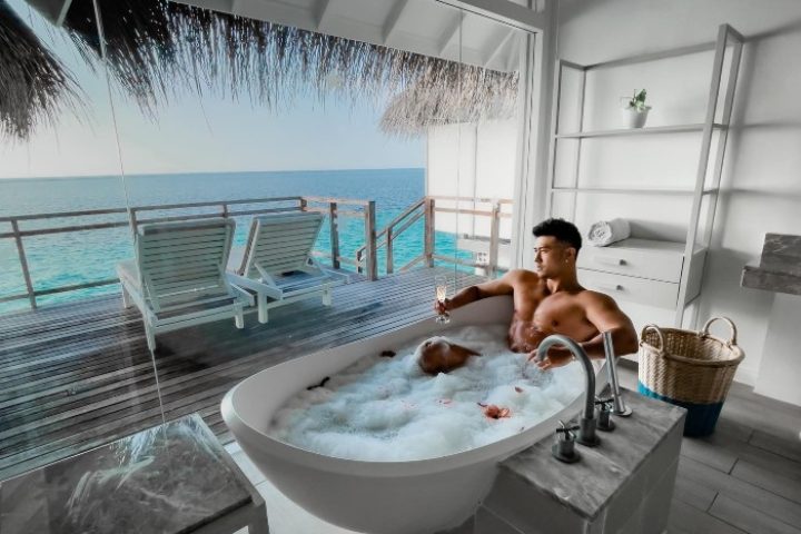 Gay honeymoon at LUX* South Ari Atoll, Maldives. Two men in a bubble bath with ocean view from water villa. Luxury travel destination.