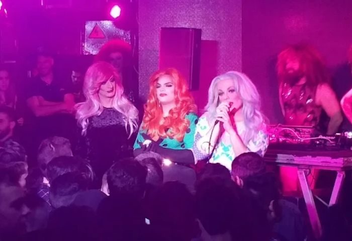 Drag queens perform at La Boite Gay Club in Madrid. A crowd watches the stage in the purple-lit nightclub. Gay travel advice.