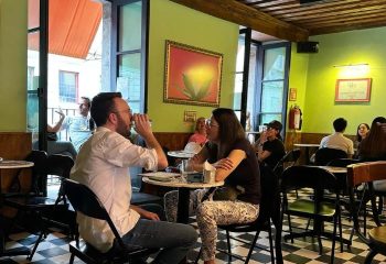 Patrons at La Botica Gay Bar in Mexico. A couple sits at a table, drinks in hand, enjoying the vibrant atmosphere. Gay travel.