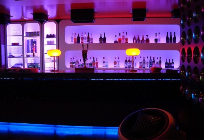 Interior of La Bulle Gay Bar, Gran Canaria. Bar with liquor bottles, purple lighting, and a unique, modern design. Gay travel destination.