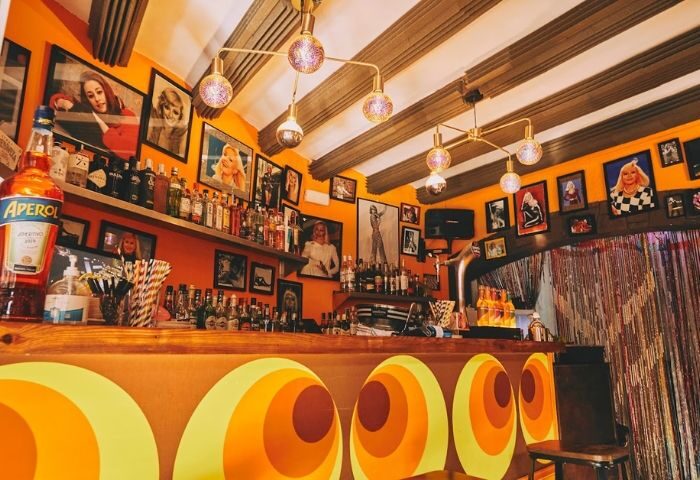 Interior of La Carra Gay Bar in Barcelona. Retro 70s design with orange walls, vintage photos, and circular patterns on the bar front.
