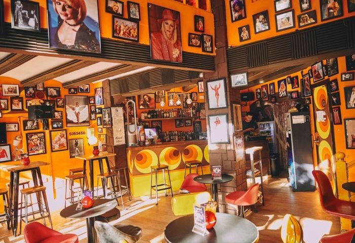 Interior of La Carra Gay Bar in Barcelona, a retro-themed space with orange walls, vintage decor, and portraits. A fun gay travel spot.