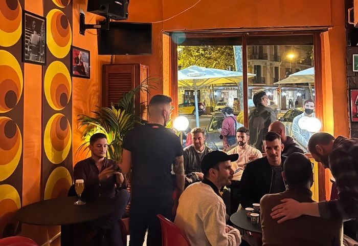 Interior view of La Carrà Gay Bar in Barcelona. Men gather at tables in a retro-styled space. Gay travel advice.
