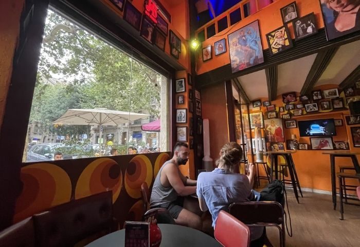 Interior of La Carra Gay Bar in Barcelona, a popular gay travel destination. People sit at tables, walls covered in pictures.