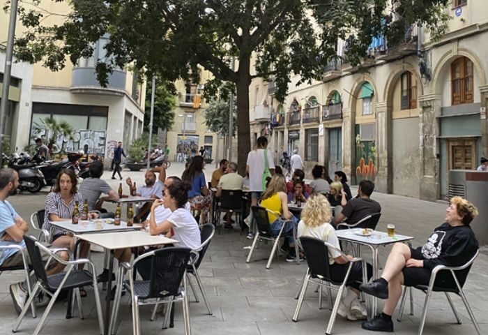 Outdoor seating at La Casa de la Pradera Gay Bar in Barcelona. People at tables under a tree. Gay travel advice in Barcelona.