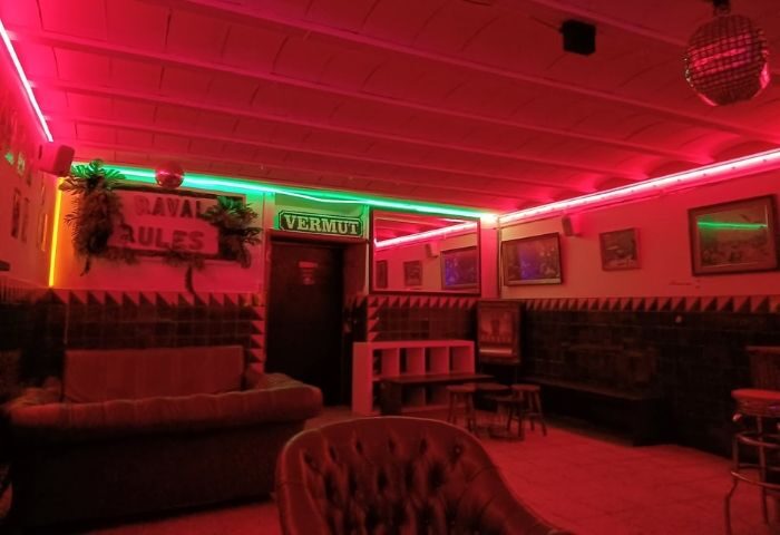 Interior of La Casa de la Pradera gay bar in Barcelona. Red lighting, disco ball, & vintage decor create a cozy, inviting space. Gay travel.