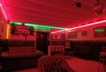 Interior of La Casa de la Pradera gay bar in Barcelona. Red lighting, disco ball, & vintage decor create a cozy, inviting space. Gay travel.