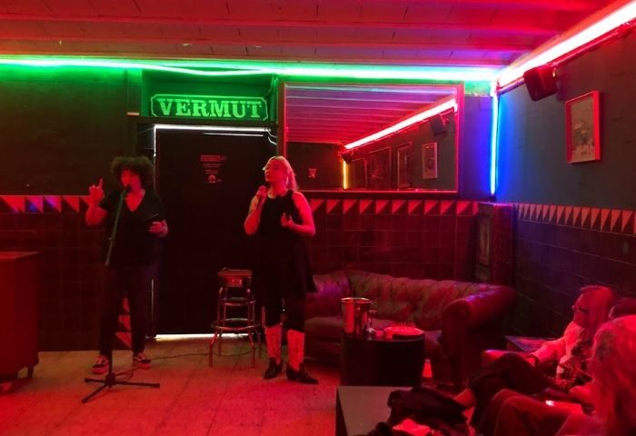 Live performance at La Casa de la Pradera gay bar in Barcelona. Performers on stage, vermut sign, and colorful neon lights. Gay travel.