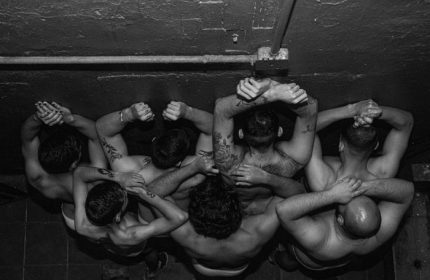 Black and white aerial view of shirtless men in La Casita CDMX gay bar, Mexico City. Tattoos visible on arms and back.