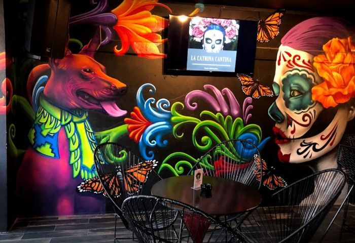 La Catrina Cantina gay bar in Puerto Vallarta. Colorful mural of La Catrina, dog, butterflies, flowers, table and chairs. Gay travel.
