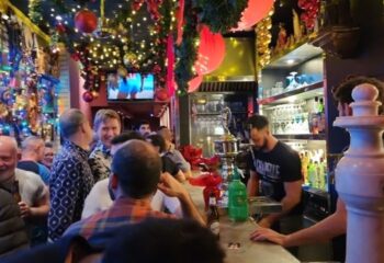 La Chapelle Gay Bar in Barcelona. Interior view of the bar with people, Christmas decorations, and a bartender serving drinks. Gay travel advice.
