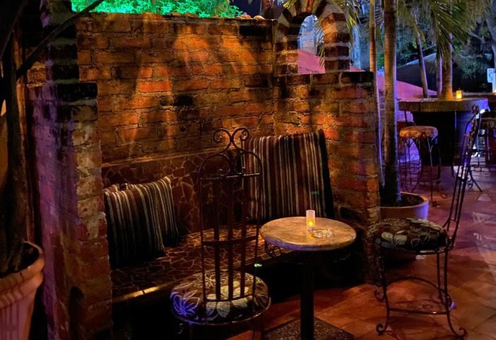 La Noche Gay Bar in Puerto Vallarta: Cozy brick seating area with pillows, chairs, and a small table. Nightlife spot for gay men's travel.