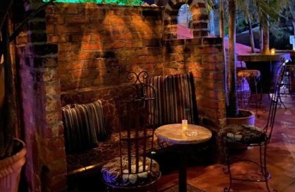 La Noche Gay Bar in Puerto Vallarta: Cozy brick seating area with pillows, chairs, and a small table. Nightlife spot for gay men's travel.