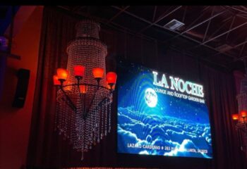 La Noche Gay Bar interior in Puerto Vallarta. Chandelier and screen showing the bar's name and address. Gay travel advice.