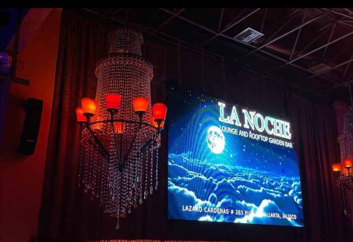 La Noche Gay Bar interior in Puerto Vallarta. Chandelier and screen showing the bar's name and address. Gay travel advice.