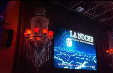 La Noche Gay Bar interior in Puerto Vallarta. Chandelier and screen showing the bar's name and address. Gay travel advice.