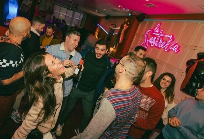 People enjoying La Sastreria gay bar in Barcelona. Gay men and women laugh and drink in a lively, inclusive atmosphere. Nightlife scene.