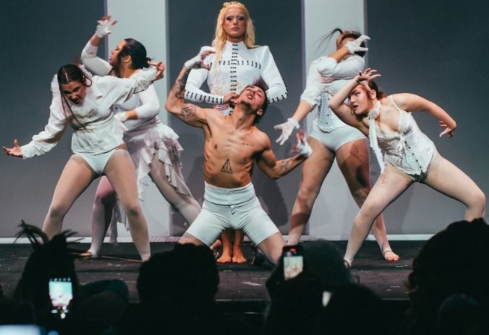 La Sastreria Cafe Gay Bar Barcelona: Performers in white costumes on stage. Drag queen, dancers, and a shirtless man entertain the crowd.