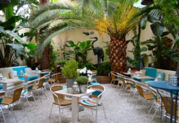 La Villa Gay Bar in Sitges: Outdoor seating area with tables, chairs, and lush greenery. A tranquil spot for gay travelers in Sitges.