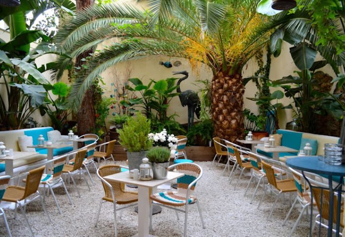 La Villa Gay Bar in Sitges: Outdoor seating area with tables, chairs, and lush greenery. A tranquil spot for gay travelers in Sitges.