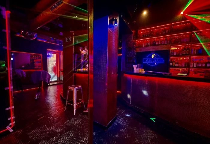 Interior of La Kama Gay Bar in Madrid. Red and blue lighting, bar with bottles, dance floor. Gay travel nightlife.