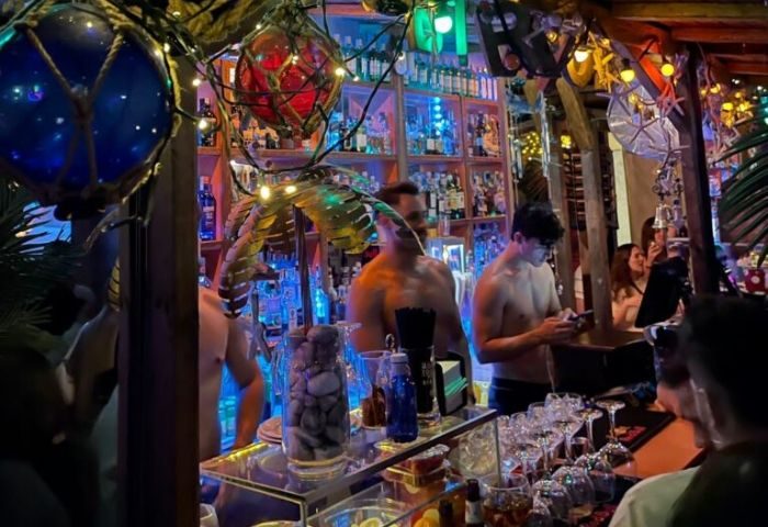 La Kama Cafe, a gay bar in Madrid. Shirtless bartenders serve drinks in a lively, decorated space. Gay travel advice.