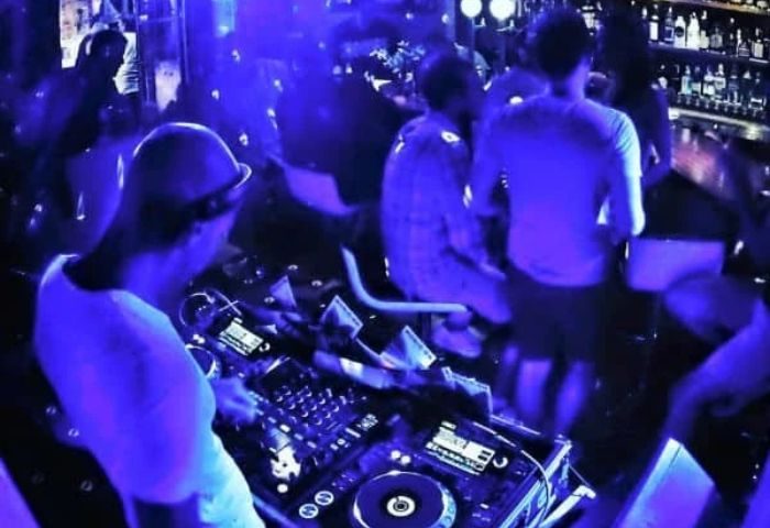 DJ at Lady D. Gay Bar in Ibiza, Spain. Nightlife scene with people dancing under blue lights. Gay travel destination.