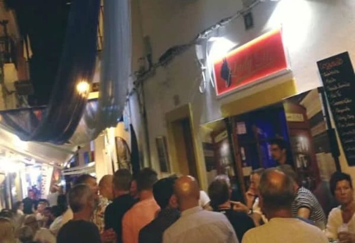 Night scene at Lady D. Gay Bar in Ibiza. Crowded street with people, bar sign, and outdoor seating. Gay travel destination.