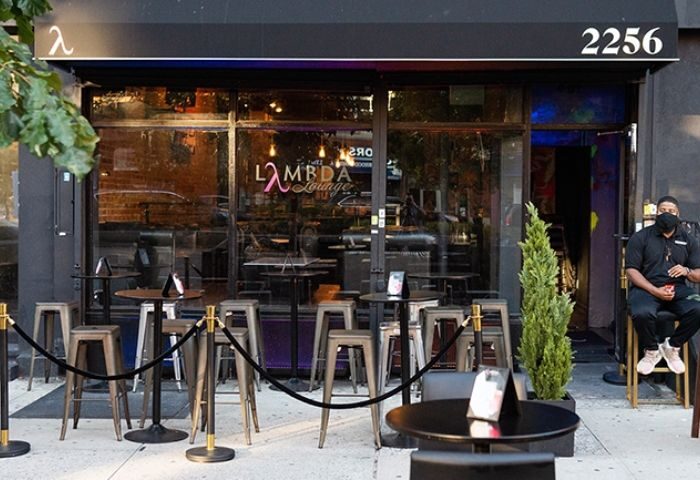 Lambda Lounge, a gay bar in New York, features outdoor seating. A masked bouncer sits by the door of this LGBTQ+ friendly spot.