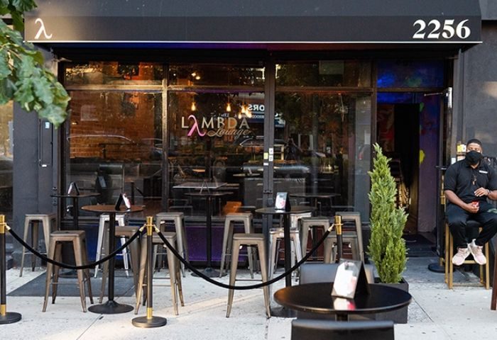 Lambda Lounge, a gay bar in New York, features outdoor seating. A masked bouncer sits by the door of this LGBTQ+ friendly spot.