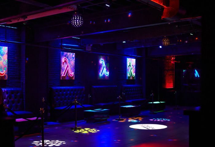 Lambda Lounge gay bar in New York. Interior view with neon Lambda signs, leather seating, and colorful lighting effects on the dance floor.