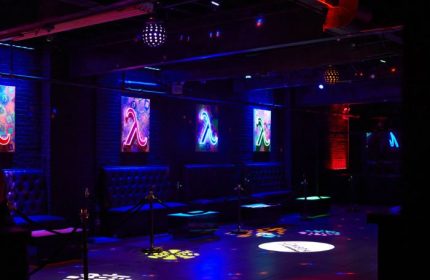 Lambda Lounge gay bar in New York. Interior view with neon Lambda signs, leather seating, and colorful lighting effects on the dance floor.