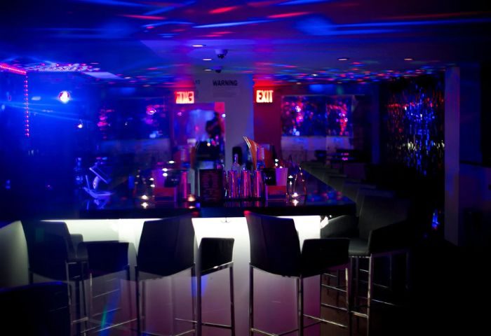 Lambda Lounge gay bar in NYC. Bar stools line the bar with a white front panel. Blue and red lights illuminate the ceiling.