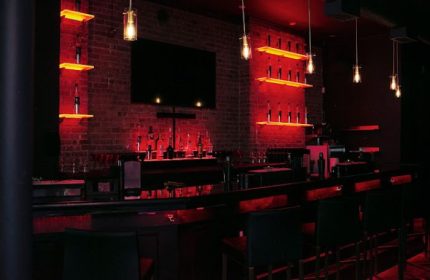 Lambda Lounge gay bar in New York. Bar with red lighting, brick wall, shelves with bottles, and hanging lights. Gay nightlife.