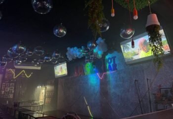 Interior of Laser Hot Bar, a gay bar in Cancun, Mexico. Disco balls hang from the ceiling. TVs play videos. Neon sign.